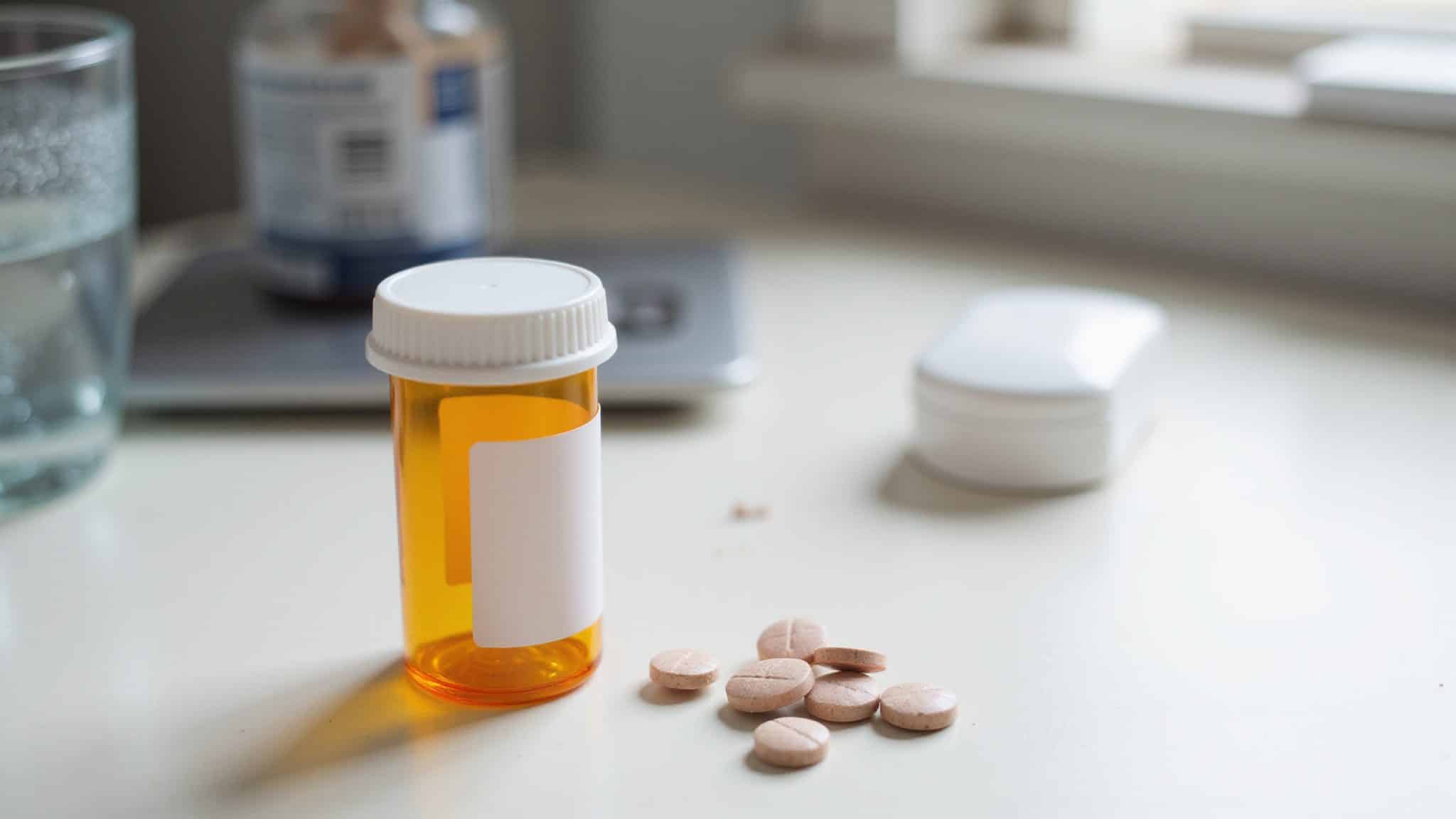 Pill bottle with scattered medication on a cluttered desk.